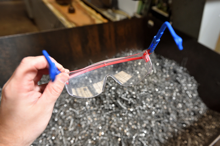 A man's hand holds a protective transparent glasses in the factory against a background of metal chips.の写真素材