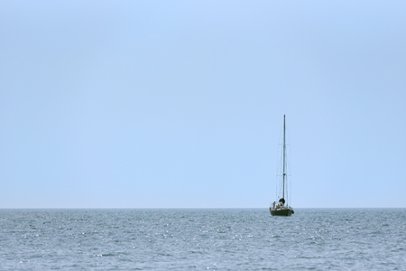 A small sailing ship with sails down, one at sea.の写真素材