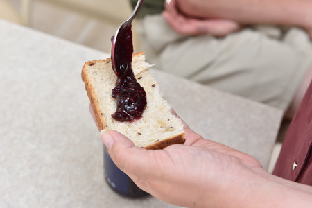 Blueberry jam with a spoon put on a piece of bread, which lies in the hand.