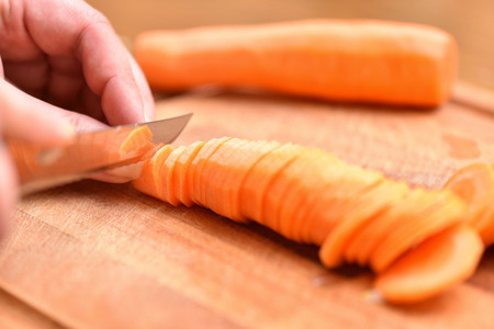 Carrot cutting. Female hands with a knife chop the carrots on a cutting board. Close-up.の写真素材