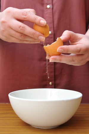 Female hands separate the egg white from the yolk over a bowl in the kitchen.