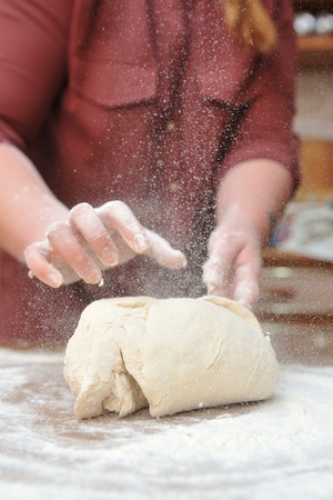 Women's hands knead the dough in the kitchen on the table. Close-up.