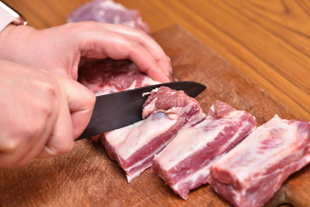 Cutting pork meat with a black knife, close-up, on a cutting board. Pork meat ribs.の写真素材