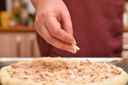 Female hand lay ingredients on raw pizza, cooking pizza.の写真素材