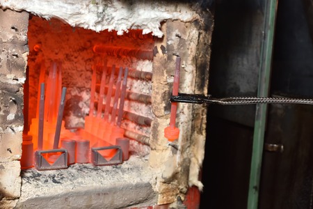 Worker pulls out the heated parts with tongs from an electric furnace for hardening metal. Work with...