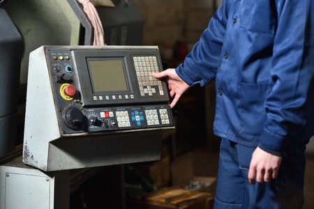 Worker in blue workwear holds hands on the control panel of the CNC machine.の写真素材