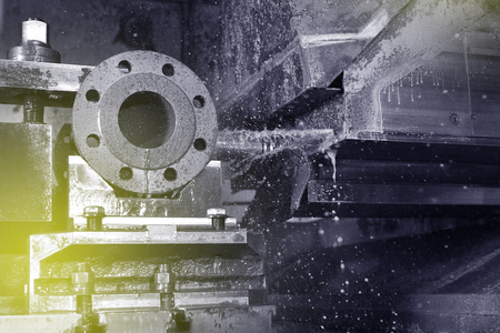 The process of drilling and grinding holes in the body of the valve on the CNC machine. Yellow-green coolant splashes into place. Close-upの写真素材