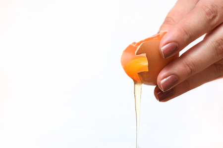 Broken egg, yolk and protein flows down on a white backgroundの写真素材