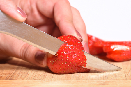 Hands of a girl is cutting fresh strawberries on kitchen counter preparing them to be blended with bananas for a smoothie or cake decorationの写真素材