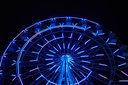 Glowing ferris wheel in an amusement park against a black night sky.の写真素材