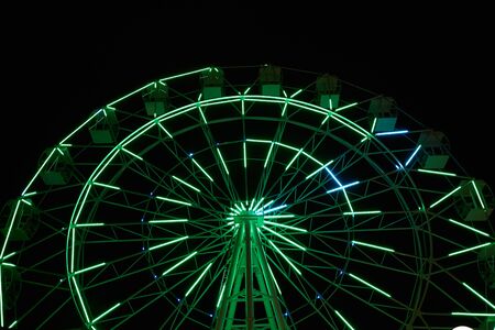 Glowing ferris wheel in an amusement park against a black night sky.の写真素材