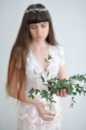 A portrait of a young girl who holds eucalyptus branches inserted into a glass transparent small vase.の写真素材