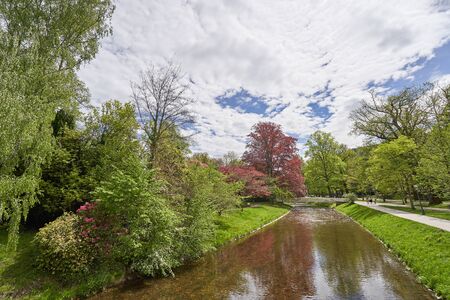 Landscape with a narrow river, trees and an iron bridge in a public park in the European city of...