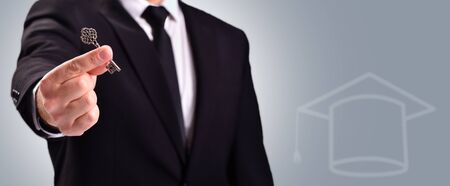 Education concept. A man in a suit holds a door key on a gray backgroundの写真素材