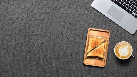 A delicious sandwich, a coffee mug and a laptop on a black table. Work break and foodの写真素材