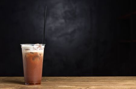 Iced coffee with ice and cream in a plastic glass on a black backgroundの写真素材