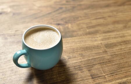 Blue mug of coffee with foam on a wooden tableの写真素材