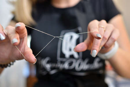 The cosmetologist holds a thread to correct the plucking of the eyebrows
