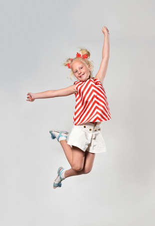 Girl child 7 years old in red striped clothes jumping cheerfully on a gray backgroundの写真素材
