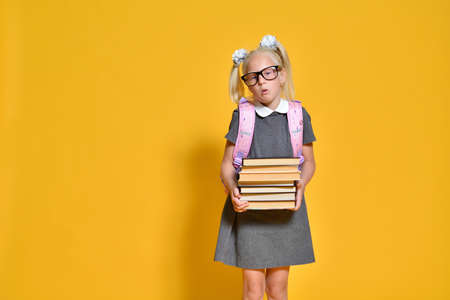Girl Elementary school student stands displeased with a stack of heavy booksの写真素材