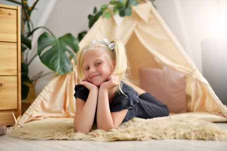 Little girl with a smile in her room on the floor next to the wigwam tentの写真素材