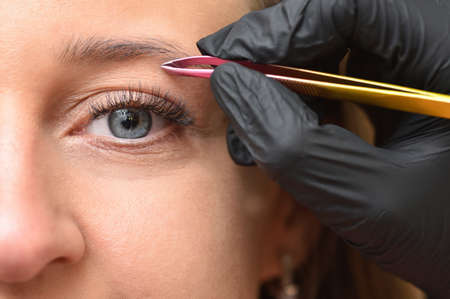 Young woman makes eyebrow correction with tweezers. Eye and tweezers close up