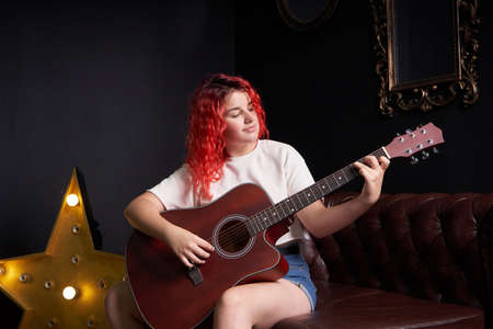 Teenage girl musician with red hair learns to play the guitarの写真素材