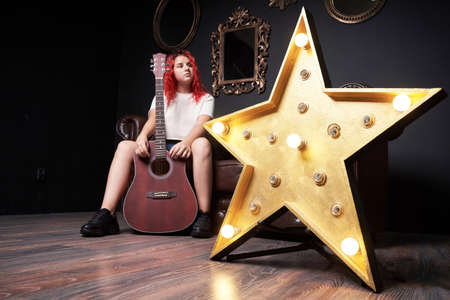 Big star with light bulbs and on the background a teenage girl with a guitar dreams of becoming a...