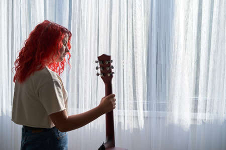 Teenage girl standing by the window and holding a guitarの写真素材