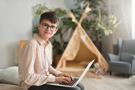 Teenager boy with glasses holding laptop on his lap and looking at the cameraの写真素材