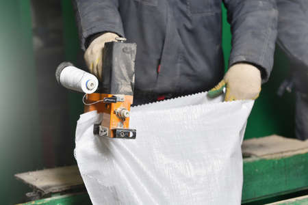 Worker sews up a white polypropylene bag with a sack sewing machine