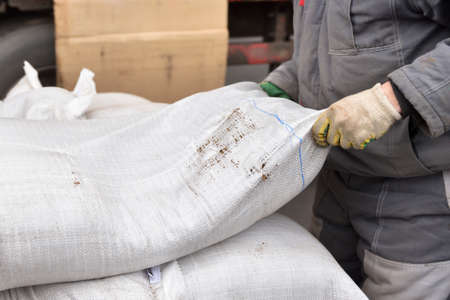A man loader at a factory raises a heavy bag with his handsの写真素材