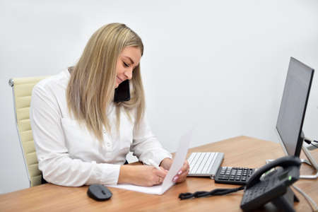 Blonde woman in the office talking on the phone and writing in a notebook