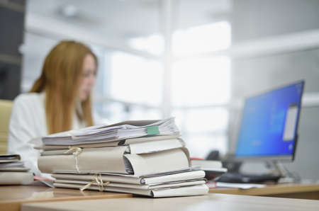 A large stack of papers in the office lies on the desk of a busy woman office managerの写真素材