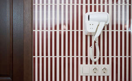A white hair dryer hanging on tiled wall in a bathroomの写真素材