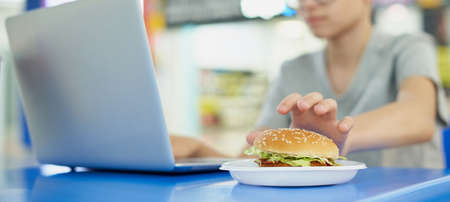 Teenager eating burger in fast food restaurant and using laptopの写真素材