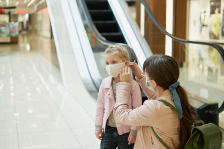 Mom puts a protective mask on a child in a shopping centerの写真素材