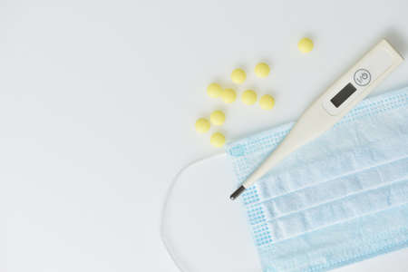 Electronic thermometer, medical mask and pills on a white background