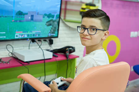 STARIY OSKOL, RUSSIA - NOVEMBER 6, 2020:Teenager with glasses sits in front of the monitor and plays a game in a hair saloonのeditorial素材