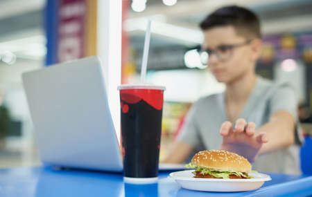 Teenage boy takes a burger while having lunch in a restaurant. Child and unhealthy fast foodの写真素材