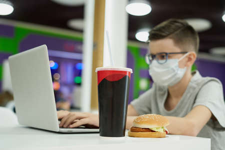 Teenage boy in face mask in fast food restaurant will eat unhealthy foodの写真素材