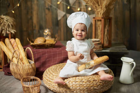 Adorable little baby baker with a French baguette in a rustic interiorの写真素材