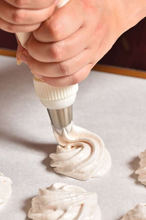 Housewife makes homemade meringues and squeezes out cream, hands close-up