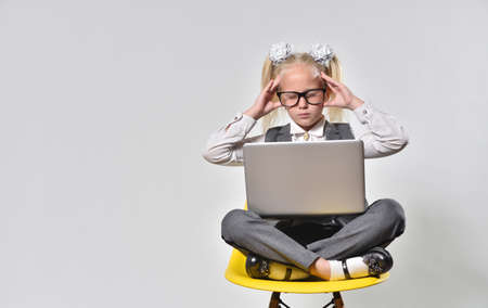 Girl child experiences stress while working at a laptop on a gray background