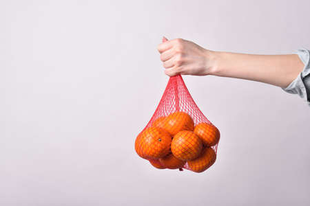 Mesh with tangerines in a female hand on a white backgroundの写真素材