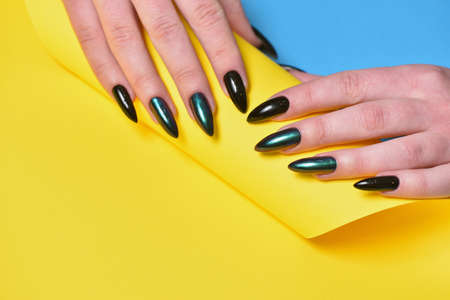 Female hands with new manicure and dark nail polish on yellow backgroundの写真素材