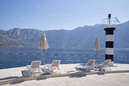 Empty sun loungers by the sea next to the lighthouse in Montenegro.