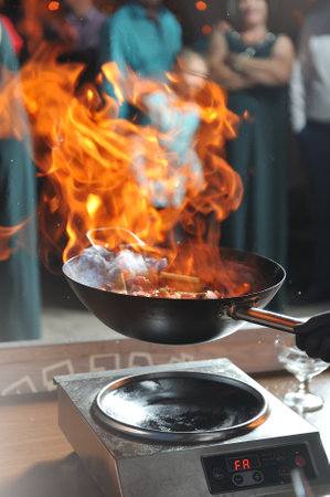 Cooking show by the chef with fire, fries meat in a frying pan and people looking itの写真素材