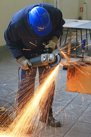 Worker grinding a metal part with grinding wheel, lots of sparks in factoryのeditorial素材