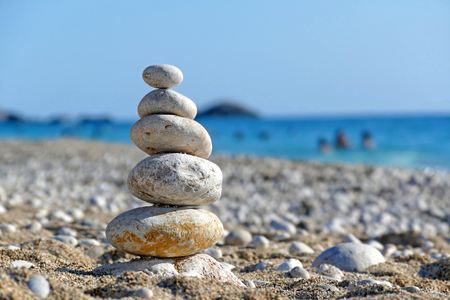 Stones balance on beach, people sunbathe, swim and enjoy on sea vacationの写真素材